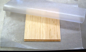 Place the plywood between sheets of waxed paper and place on a hard, flat surface.